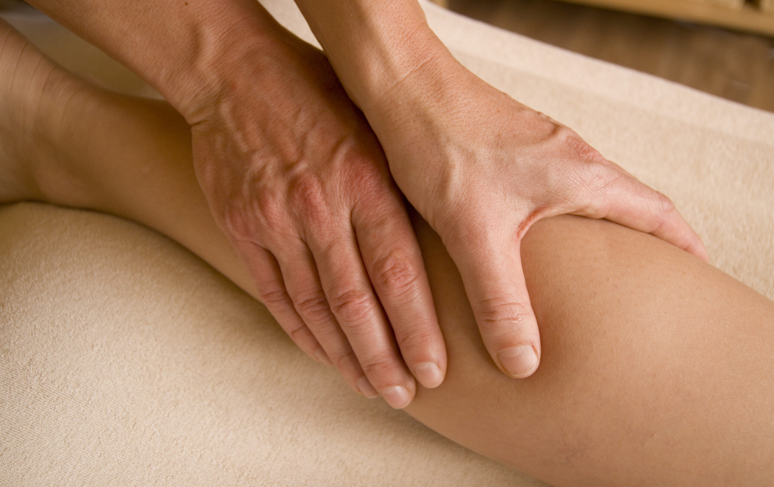 Handen van een massagetherapeut die de kuit behandelt tijdens een massagetherapie-sessie.